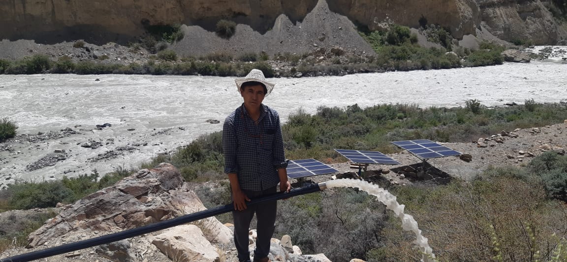 Farmer standing near a solar water pump installation by a river
