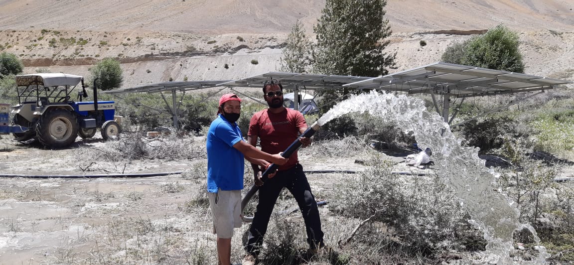 Customers holding a water pump outlet with solar panels in the background